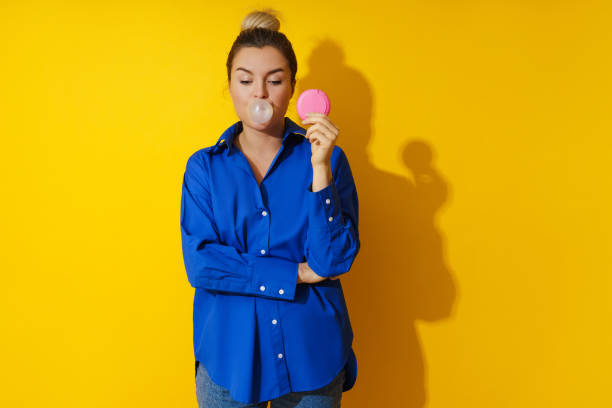 mujer feliz soplando una burbuja con chicle sobre fondo amarillo - chewing gum women bubble blowing fotografías e imágenes de stock