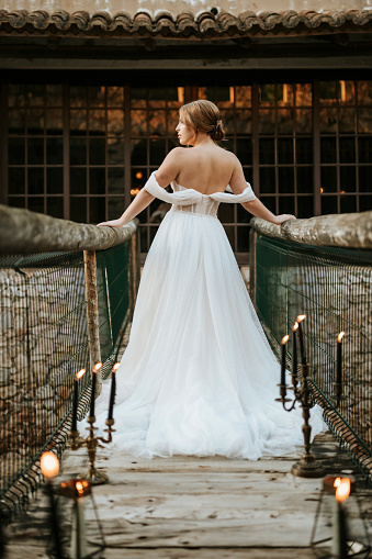 Beautiful rustic bride seen from profile standing on wooden bridge full of candles