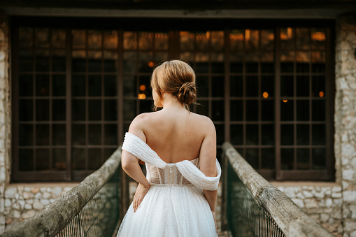 Back of bride standing on wooden bridge in rustic arrangement