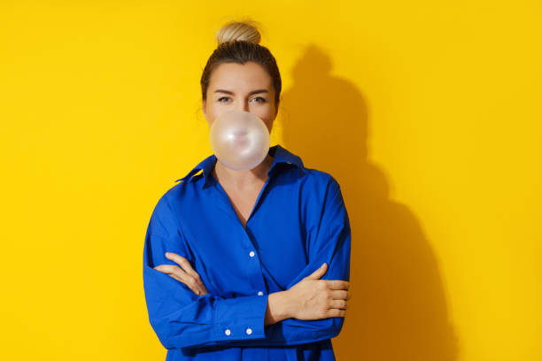 mujer feliz soplando una burbuja con chicle sobre fondo amarillo - chewing gum women bubble blowing fotografías e imágenes de stock