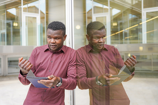 African businessman outside the office with a tablet and his reflection in the glass