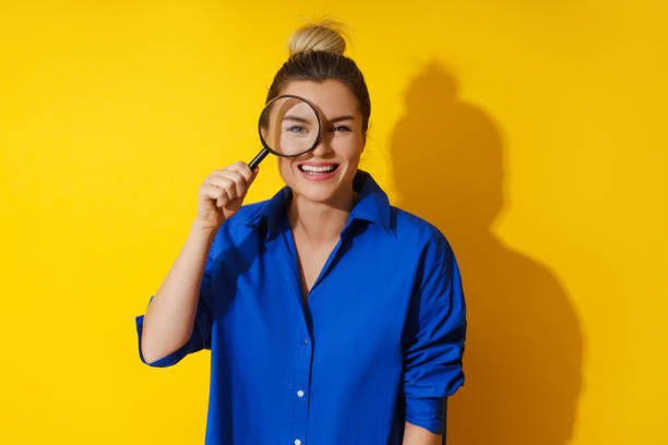 Curious woman is peering through magnifying glass with great interest, examining something closely stock photo