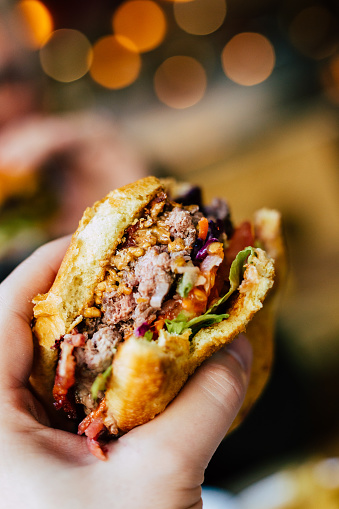 Close up image depicting the personal perspective of a man holding a fresh burger loaded with beef and crispy bacon and salad. Room for copy space.