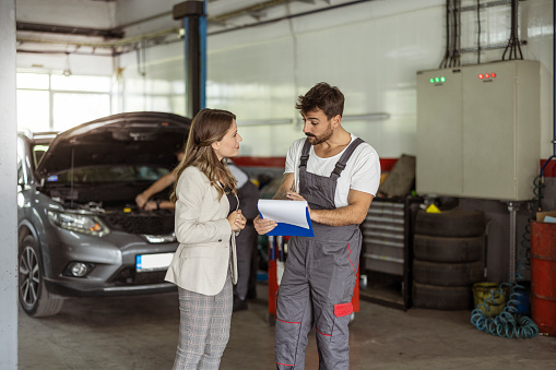 Mechanic with clipboard and customer or car owner at workshop. Auto service, repair, maintenance and people concept