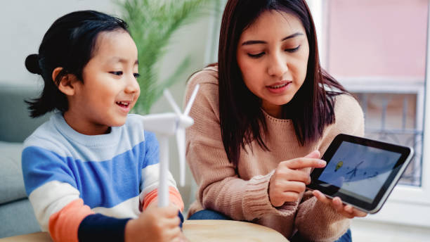 bambino asiatico che impara l'energia sostenibile a scuola a casa - focus sul volto della madre insegnante - child digital tablet mother teaching foto e immagini stock