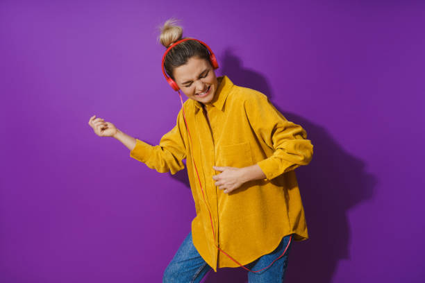 Cheerful girl wearing yellow shirt listening music using red headphones and playing air guitar against purple background Portrait of young cheerful girl wearing yellow shirt listening music using red headphones and playing air guitar against purple background air guitar stock pictures, royalty-free photos & images