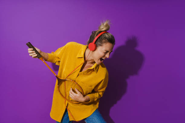 Cheerful girl is jamming out in her yellow shirt while wearing red headphones. She's strumming away on her racket like it's a guitar. stock photo