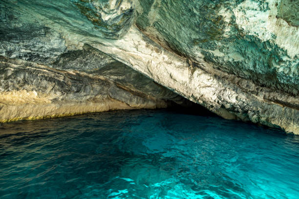 Beautiful entrance in an amazing sea cave in Greece. The water is turquoise and clear. The stone cave walls are rough and covered in green moss. The sea is calm.