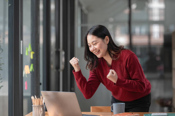 istock Asian woman celebrates winning or getting e-commerce shopping offer on computer laptop. Excited happy girl winner looking at notebook celebrating success. 1461621102