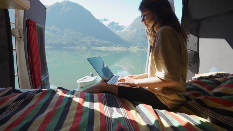 Woman working with laptop in camper van near the lake