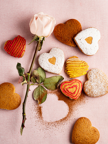 Stock photo showing elevated view of plate containing a cut, heart-shaped red velvet cake covered in butter cream and decorated with dehydrated raspberry powder and sugar sprinkle hearts, displayed against a yellow background.