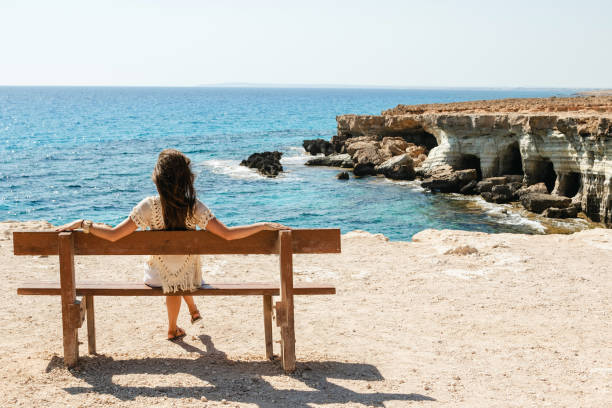 woman sits on a bench near sea cliffs at cape greco viewpoint, enjoying the scenery and natural beauty. - famagusta imagens e fotografias de stock