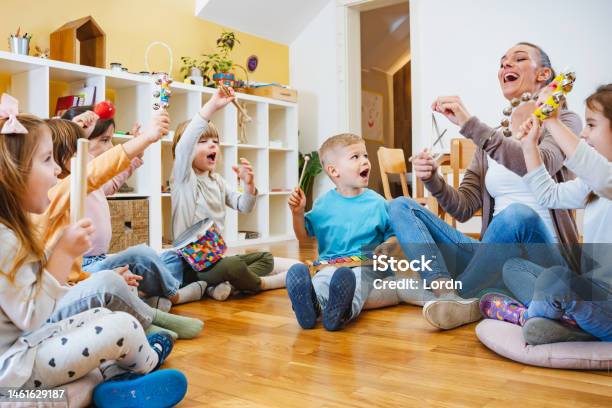 Kindergarten Teacher With Children Sitting On The Floor Having Music Class Using Various Instruments And Percussion Stock Photo - Download Image Now