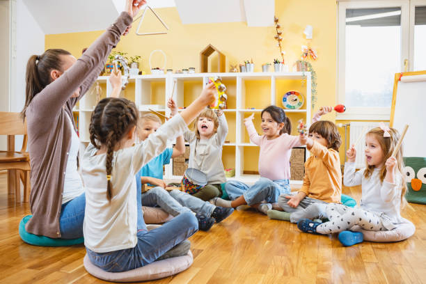 istock Kindergarten teacher with children sitting on the floor having music class, using various instruments and percussion. 1461629584