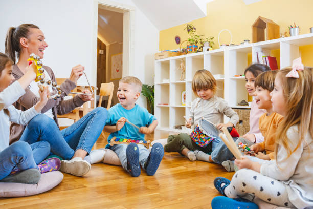 istock Kindergarten teacher with children sitting on the floor having music class, using various instruments and percussion. 1461629598