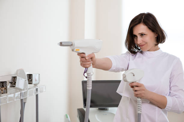 istock Professional Funny Female Doctor Posing in Doctor's Smock While Holding Two Intence Pulse Light Apparatus in Laser Rejuvelation Beauty Treatment Salon. 1461630068