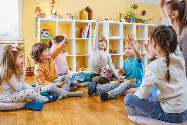 istock Kindergarten teacher with children sitting on the floor having music class, using various instruments and percussion. 1461630555