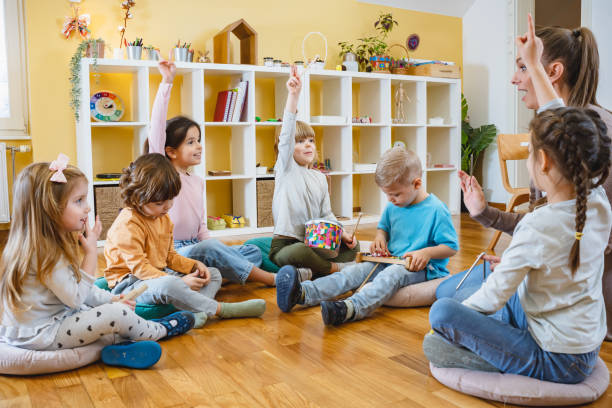 istock Kindergarten teacher with children sitting on the floor having music class, using various instruments and percussion. 1461630556