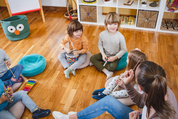 istock Kindergarten teacher with children sitting on the floor having music class, using various instruments and percussion. 1461631154
