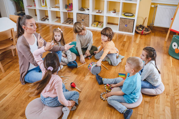 istock Kindergarten teacher with children sitting on the floor having music class, using various instruments and percussion. 1461631410