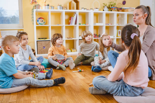istock Kindergarten teacher with children sitting on the floor having music class, using various instruments and percussion. 1461631418