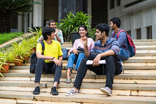 Group of happy students having chat with talking each other while sitting on college campus - concept of friendship, break time and communication.