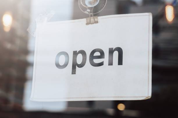 istock The black text open on the simple white plain paper stick on the transparent mirror glass door to announce and notice people that this restaurant, cafe and shop is open after lockdown and corona virus pandemic, blur background 1461634419