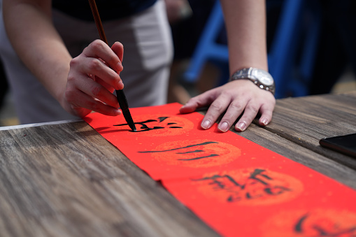 Cropped image hand of asian Chinese male practising Chinese calligraphy for Chinese new year celebration home decoration purpose with prosperity and good wording on a red piece of paper