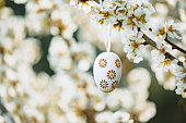 Floral easter egg in beige and brown tones hanging in between almond blossoms on an almond tree on the island Mallorca