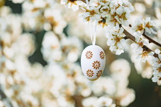 Floral easter egg in beige and brown tones hanging in between almond blossoms on an almond tree on the island Mallorca stock photo