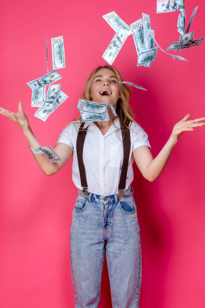 istock Caucasian Girl Posing WIth Bunch of Flying Falling American Currency banknotes While Posing With Smile Against Coral Background. 1461636238