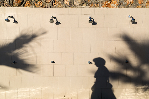 The shadow of a woman passing by an outdoor shower on the beach by the sea, copy the space