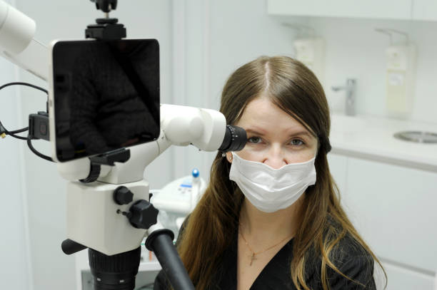 istock Big screen tablet young dentist sits near microscope for dental treatment research prosthetics filling canals teeth long hair black dress code white background latest technology equipment microscope 1461641940