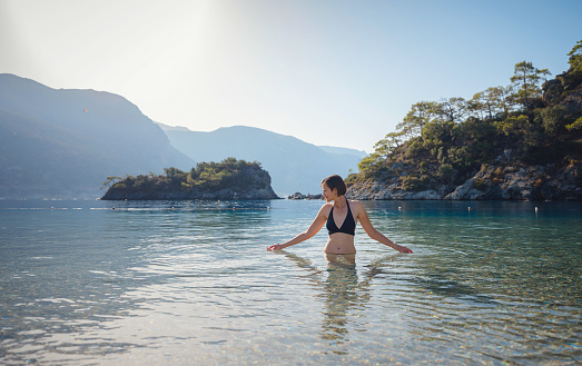 Summer lifestyle portrait of Happy traveller woman in black swimsuit enjoys her tropical beach vacation in Oludeniz Blue Lagoon Turkey.