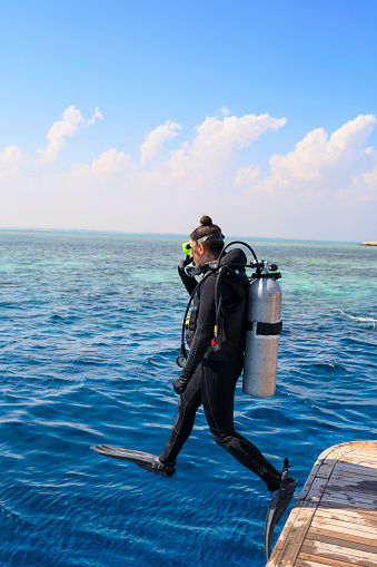 Water sports. Pretty scuba diver, attractive women, jumping to go scuba diving.  Sporting women. Beautiful blue sea in the background.