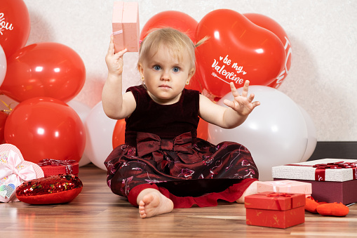 Cute little girl opens gifts sitting among the balls. Children and Valentine's Day