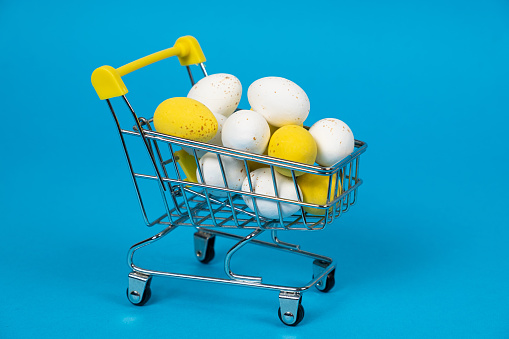 Easter white and yellow quail painted eggs in a shopping cart on a blue background. Easter Sale, copy space for text.