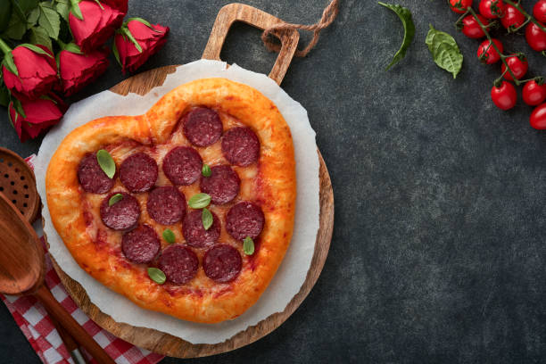 istock Valentines day heart shaped pizza with mozzarella, pepperoni and basil, wine bottle, two wineglass, gift box on black background. Idea for romantic dinner Valentines day. Top view. Mock up. 1461650825