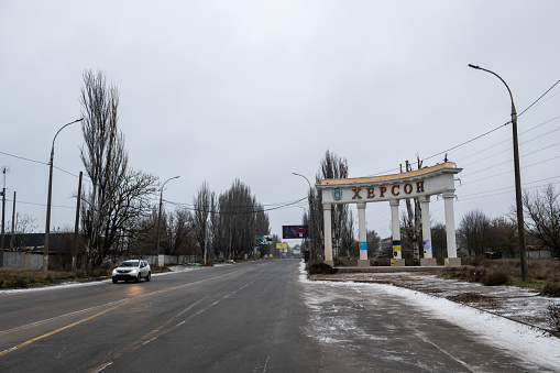 Kherson, Ukraine - December 5, 2022: On a cold winter afternoon, a car drives past the colonnaded sign marking the entrance to the city of Kherson.