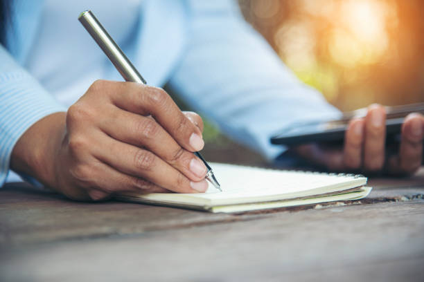 istock Man hands writing notebook diary with coffee cup and smartphone on wood desk. Close up man hands using pen sitting at wooden table outdoors lifestyle. Men write planner note diary office agenda 1461652906