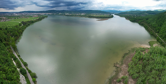 Aerial drone panorama above a lake in Valcea County, Romania. Stormy weather, rain clouds are gathering above the surrounding forests. Several small villages can be seen on the lake's shores.