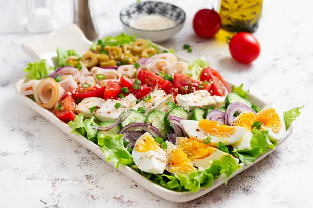 Photo of Healthy cobb salad with ham, cucumber, tomato, olives, feta cheese and eggs. Ketogenic lunch.