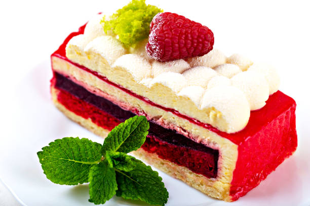 A piece of raspberry sponge cake with fluffy cream and mint on a white plate close up