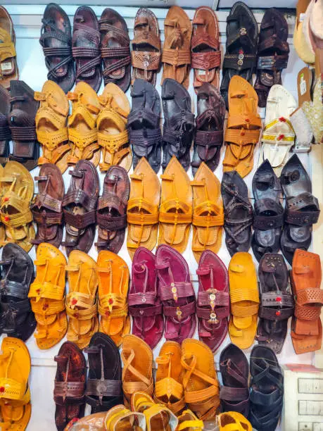 Photo of Stock photo of popular and traditional kolhapuri chappal display on wall for sale in the local shop.It is handmade leather chappal with unique design and color at Kolhapur, Maharashtra, India.
