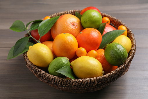 Different citrus fruits in basket on wooden table