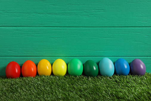 Bright Easter eggs with on green grass against wooden background