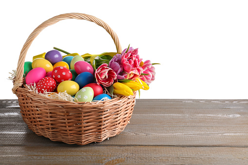 Colorful Easter eggs in wicker basket on wooden table against white background