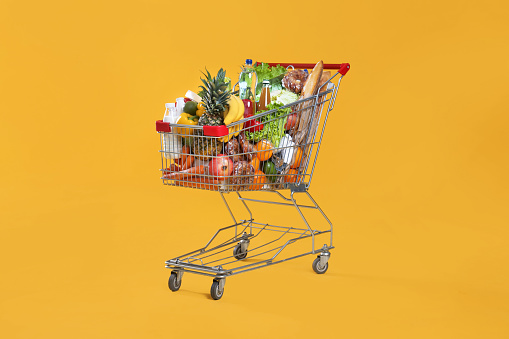 Carrito de compras lleno de comestibles sobre fondo amarillo photo