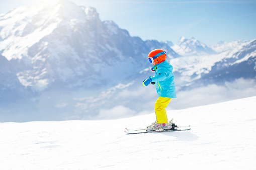 Blue and white mountain skis, sunscreen mask or ski goggles and ski boots lie on bright alpine snow. Alpine ski equipment on snow
