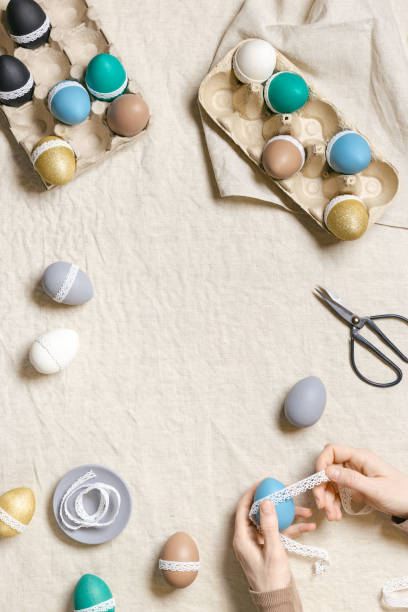 istock Decoration Easter eggs, female hands decorating colorful chicken egg with white tape lace, traditional celebration food and holiday symbol.  Home preparing for Happy Easter. Top view 1461681044